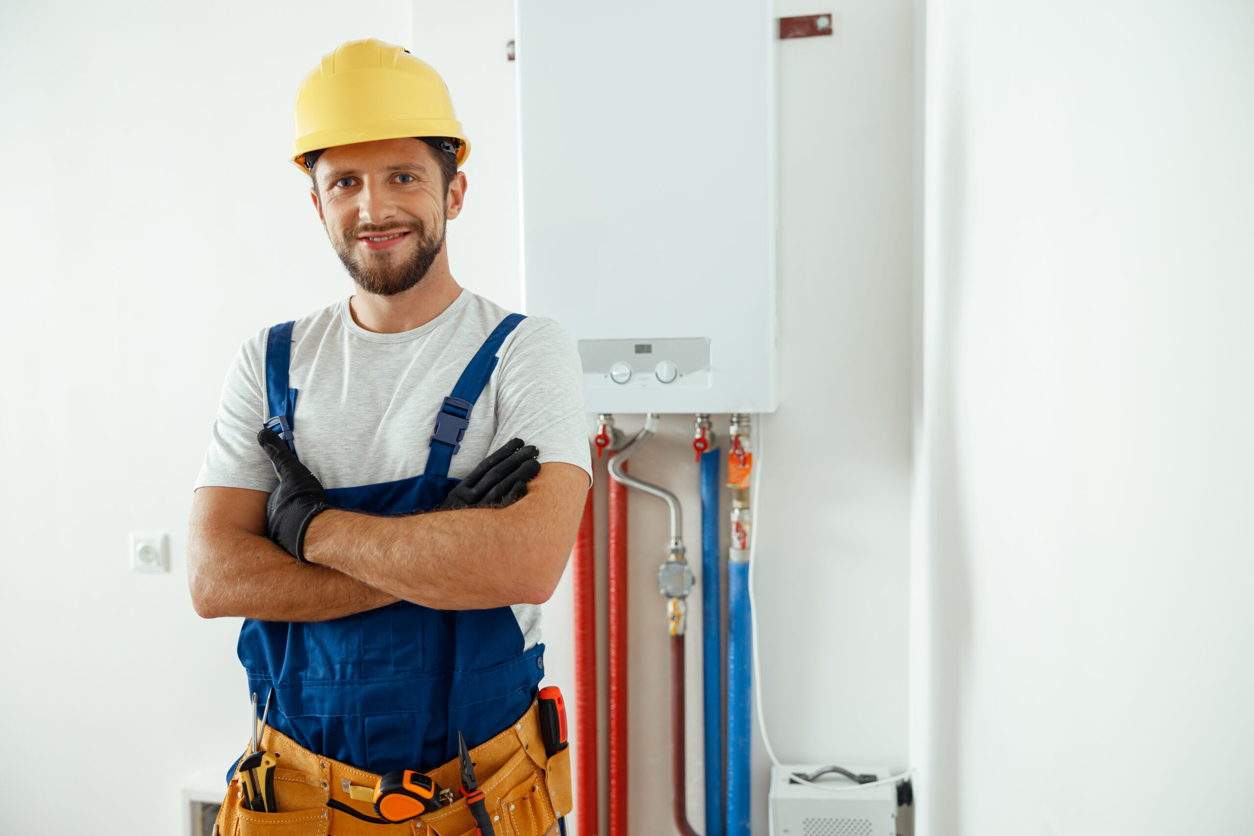 Smiling technician servicing the house heating system looking at camera while standing with arms crossed